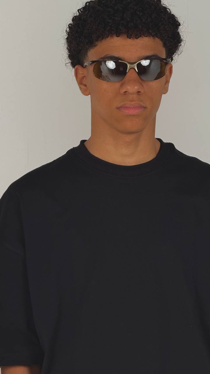 Person wearing sunglasses and a black shirt against a plain background