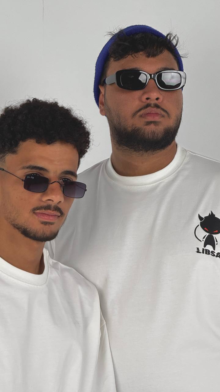 Two men wearing sunglasses and white shirts with a logo on a plain background