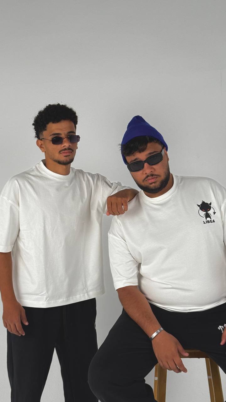 Two men wearing white shirts and black pants against a plain background