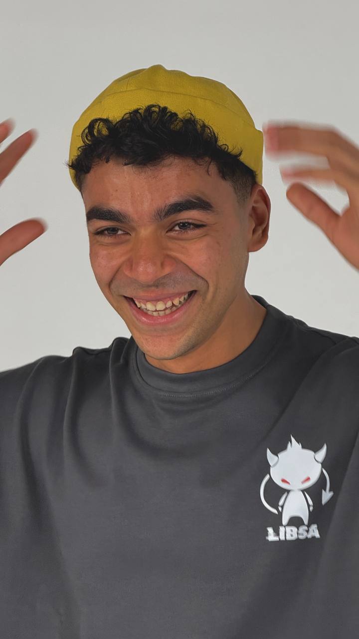 Person wearing a yellow cap and gray turtleneck with a logo, against a plain background